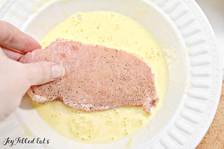 hand dipping meat in egg wash