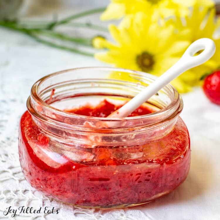 jam of sugar free strawberry jam with a small white porcelain spoon resting in it 