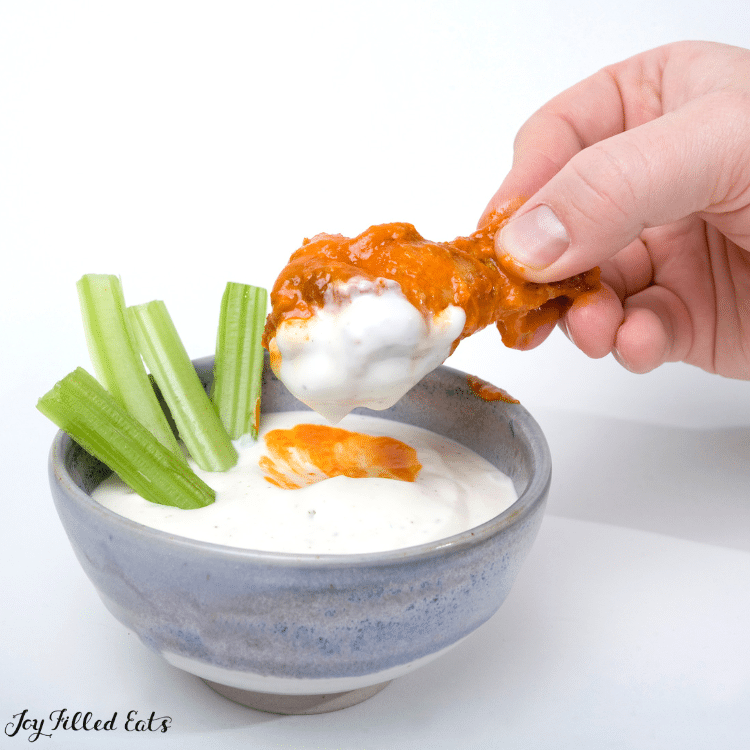 hand dipping chicken wing into dip 