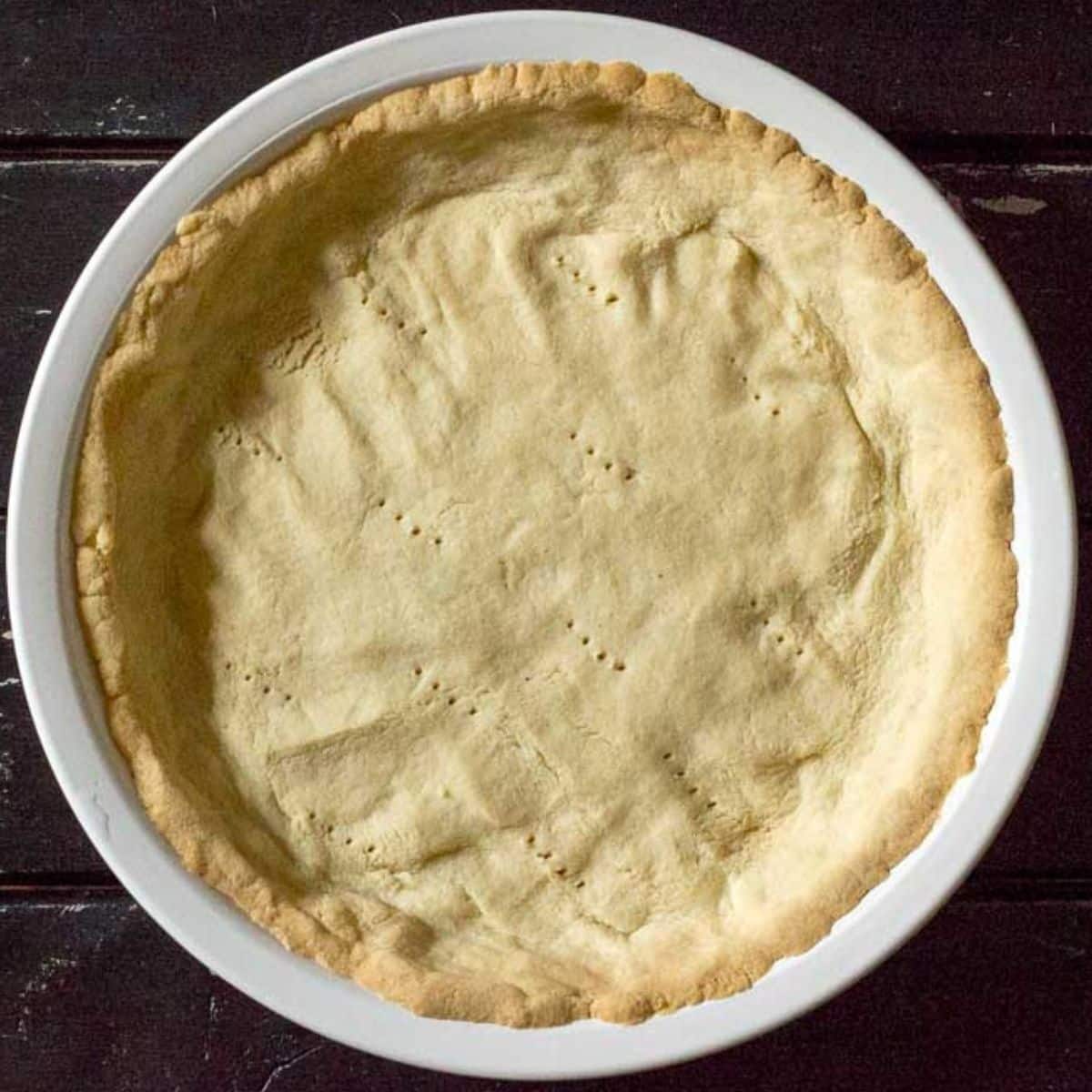 low carb keto pie crust baked into white pie plate with fork holes punched in