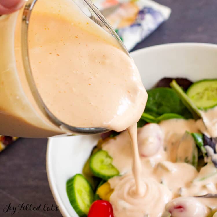 close up of keto thousand island dressing recipe being poured on top of a green salad in a white bowl