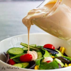keto thousand island dressing recipe being poured on top of a green salad in a white bowl