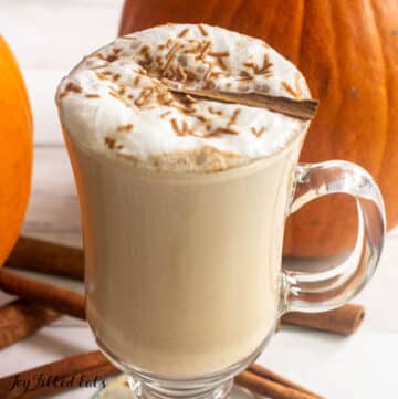 keto pumpkin spice latte recipe shown in a glass mug with cinnamon sticks and pumpkins behind