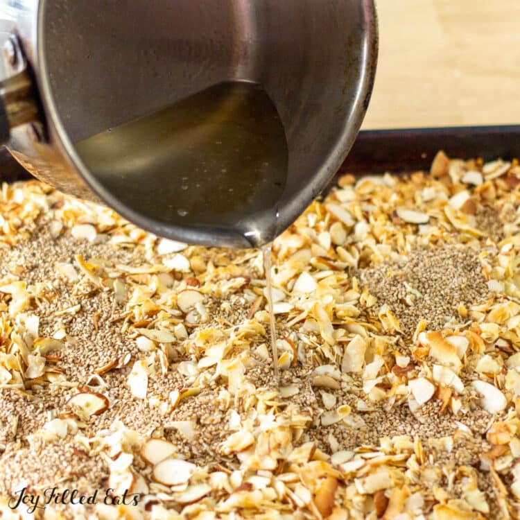 hand pouring saucepan filled with flavored sweetener onto granola ingredients laid on a sheet pan