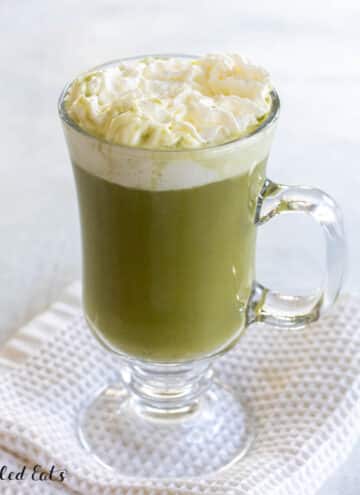 healthy matcha latte recipe topped with whipped cream in tall glass mug with handle