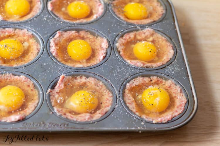 raw egg cracked on top of raw sausage in muffin tin