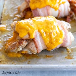 bacon wrapped stuffed chicken thighs with melted cheddar on baking pan