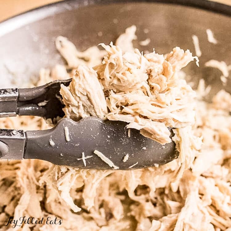 tongs lifting up shredded chicken breast