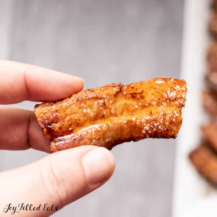 one of the air fryer pork belly slices held up by a hand