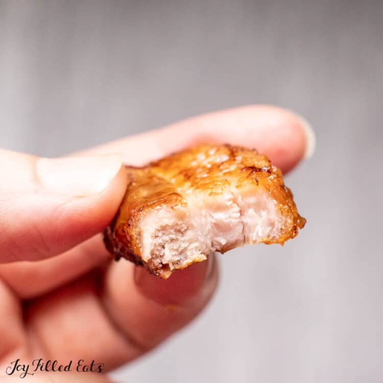 hand holding a piece of pork belly with a bite missing