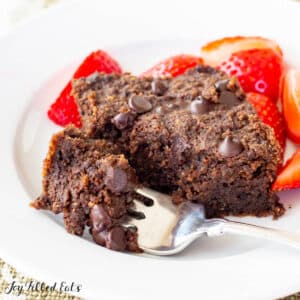 one of the low carb brownies on a plate with small bite broken off on fork. Plate also includes a side of cut strawberries