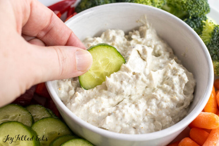 hand dipping a cucumber slice into the blue cheese dip