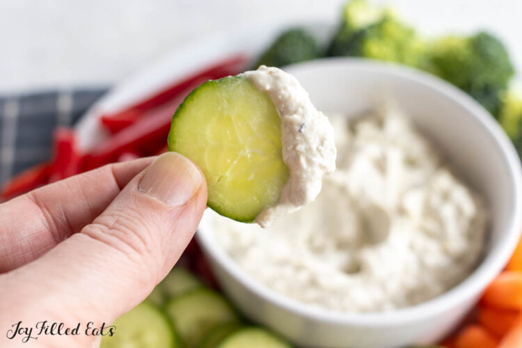 cucumber with blue cheese dip being held up by a hand