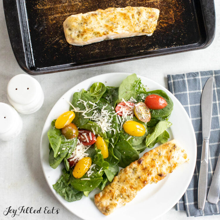 overhead shot of baked salmon with parmesan chive mayo served with a salad on a dinner plate