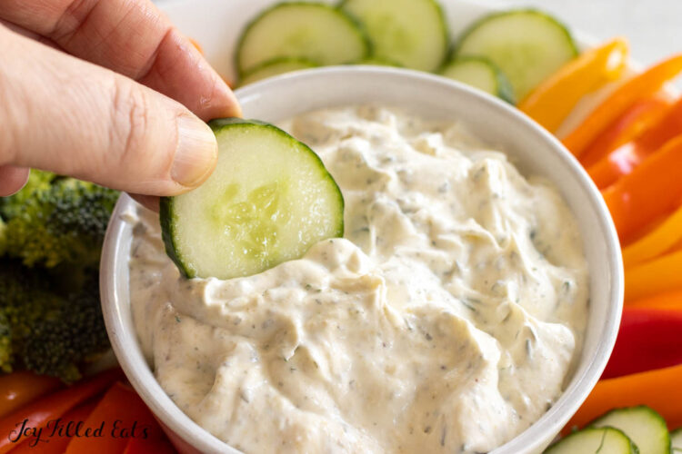 hand dipping a cucumber into the dill dip