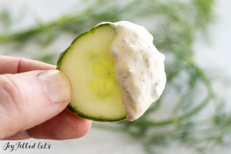hand holding up a cucumber with dill dip