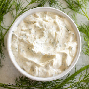 dill dip recipe in white bowl surrounded by sprigs of fresh dish