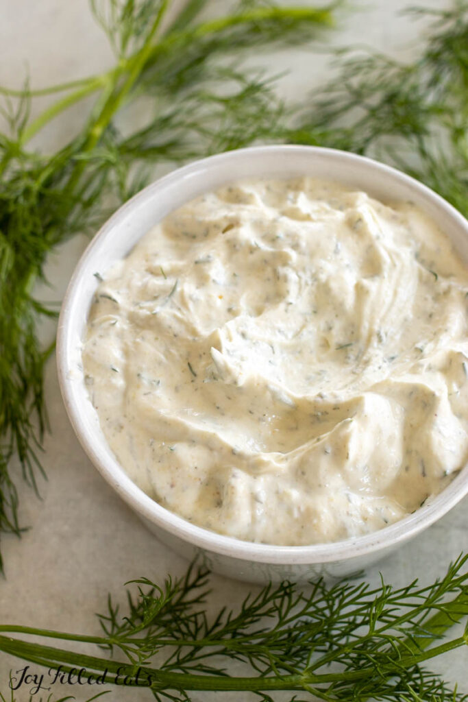 vertical shot of dill dip recipe in white bowl surrounded by sprigs of fresh dish
