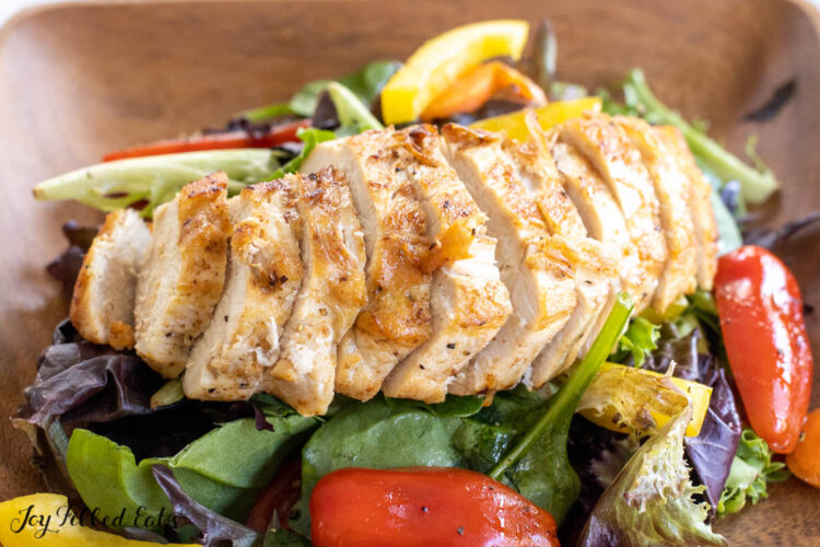 sliced butter poached chicken on top of a garden salad