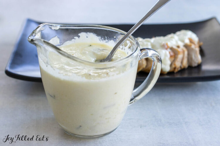 pitcher of shallot cream sauce in front of the cream sauce served over butter poached chicken