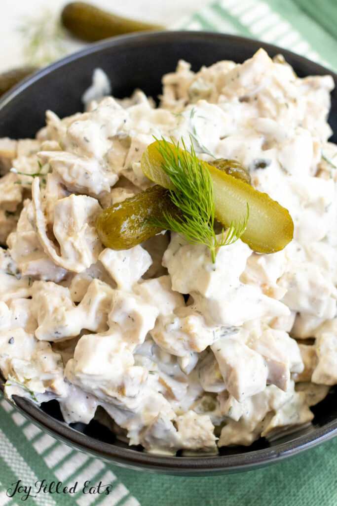 dill pickle chicken salad in a bowl topped with a halved pickle and sprig of dill