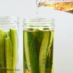 easy refrigerator pickles recipe being made with brine being poured over cucumbers in a jar close up