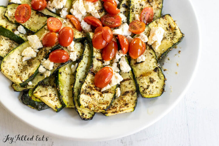 grilled greek zucchini with tomatoes and feta on a serving platter