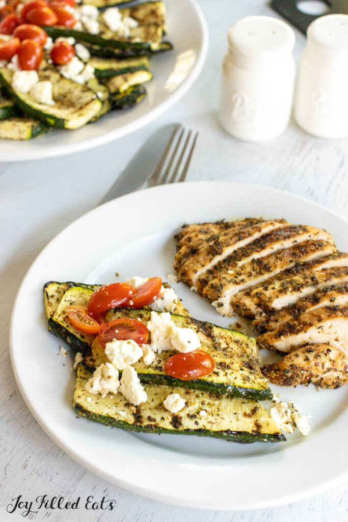 greek zucchini with tomatoes and feta on a dinner plate with grilled tuscan chicken