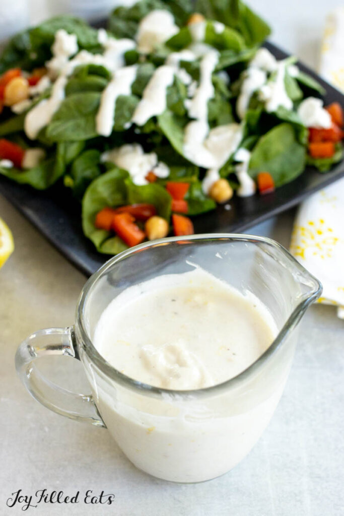 lemon yogurt dressing in a small glass pitched with a salad behind