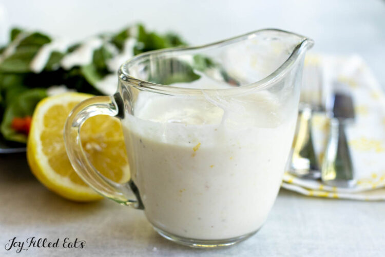 lemon yogurt dressing close up in a small glass pitched with a salad behind