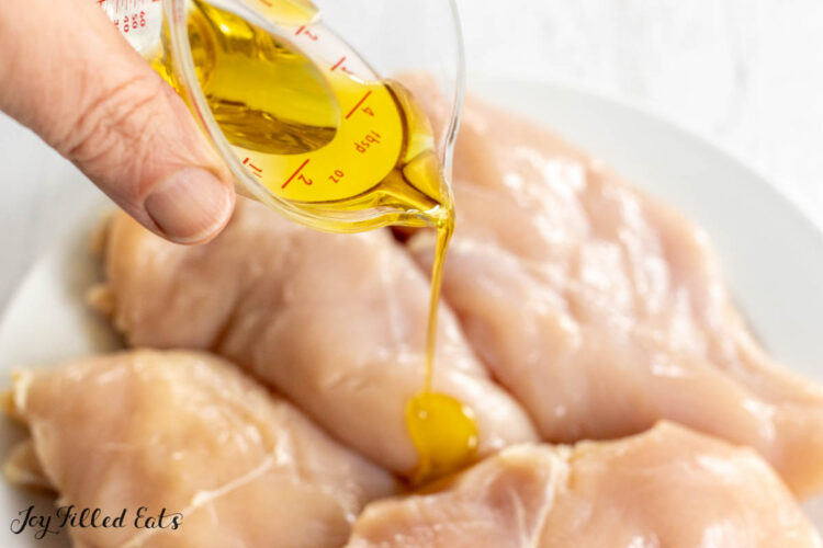hand drizzling olive oil on top of poultry