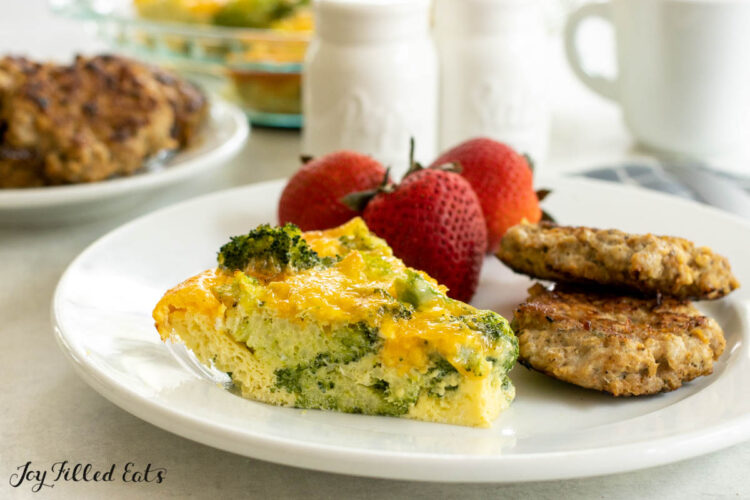 slice of the crust less broccoli quiche recipe on a plate with sausages and strawberries