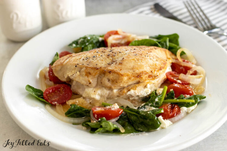 chicken breast stuffed with goat cheese on top of bed of spinach on dinner plate