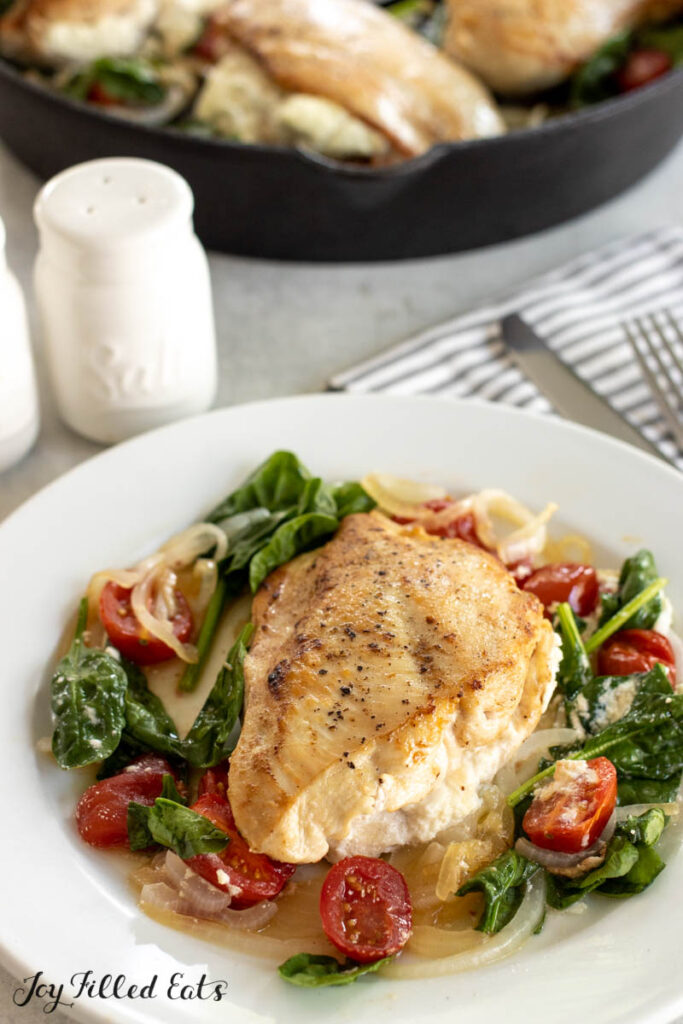 chicken breast stuffed with goat cheese on top of bed of spinach on dinner plate