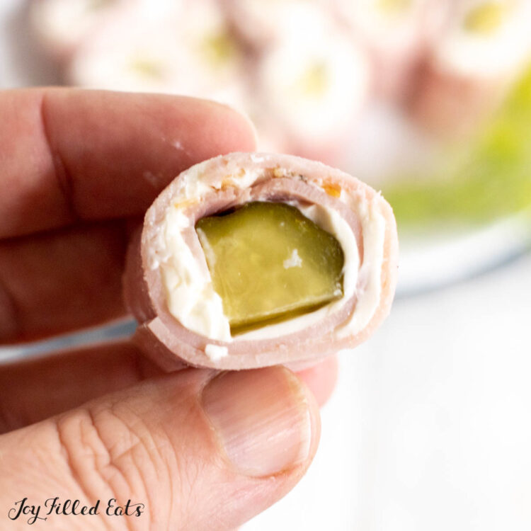 hand holding up a pickle roll up with ham