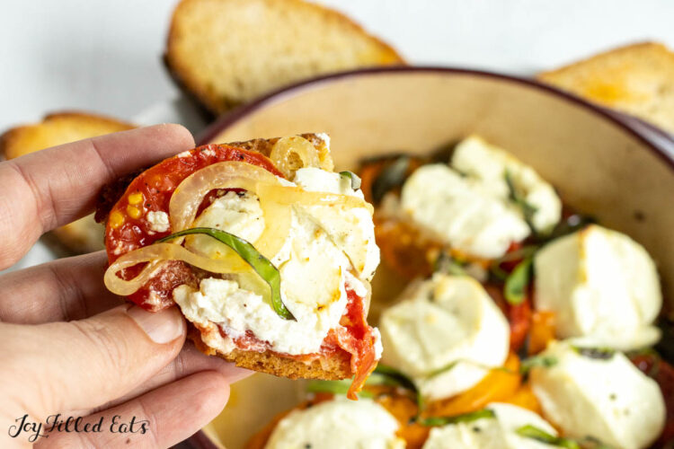 hand holding up toasted bread topped with baked goat cheese