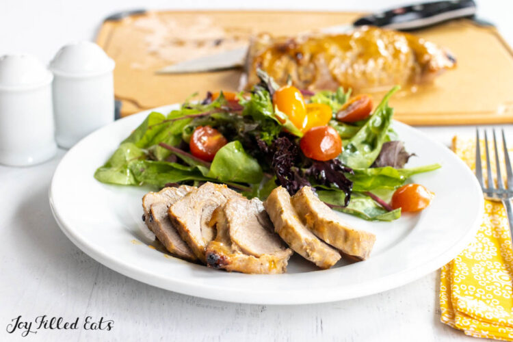 honey mustard pork tenderloin sliced on a dinner plate with a side salad
